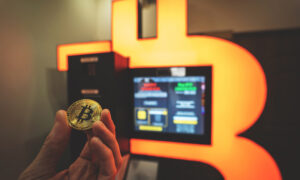 Someone holding a Bitcoin in front of a Bitcoin ATM